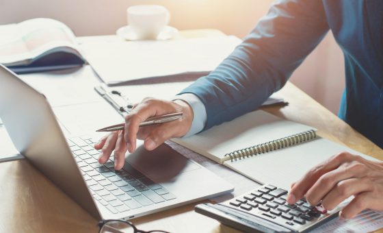 رجل أعمال يعمل في المكتب مستخدمًا الآلة الحاسبة والكمبيوتر المحمول. مفهوم المالية والمحاسبة